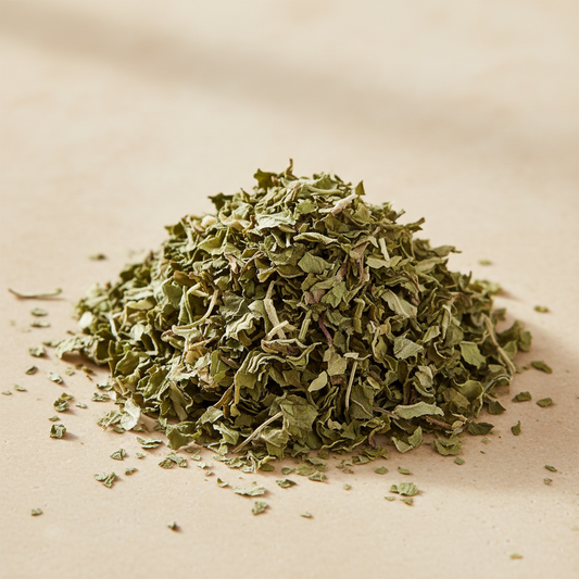 Organic dried peppermint leaf cut into curled green flakes on warm ivory stone